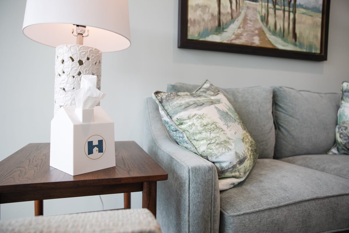 A tissue box in a Hope-branded cover on a side table next to a sofa